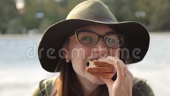 一个戴着眼镜和帽子的年轻女孩吃一个美味的三明治食物视频的预览图