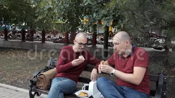 两个秃头正坐在公园里吃三明治和薯条美味的食物快餐视频的预览图
