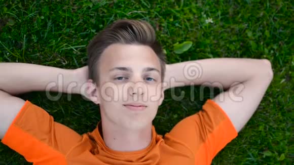 少年躺在草地上微笑着对着镜头眨眨眼双臂抱在头后视频的预览图