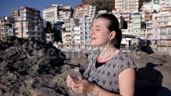 美丽的少女正在海滩上用耳机听音乐视频的预览图