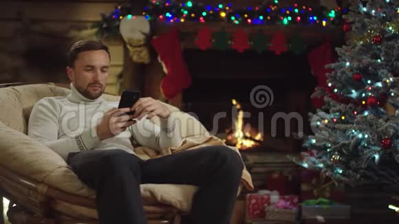 成年帅哥在圣诞夜用智能手机装饰圣诞树视频的预览图