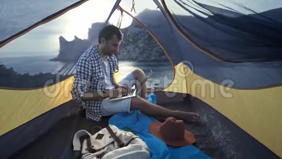 自由职业者使用笔记本电脑在海滩露营帐篷工作从事新启动项目的自由职业者视频的预览图