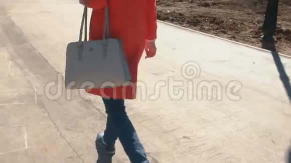 穿红色外套和运动鞋的年轻女子在春天公园散步特写腿视频的预览图