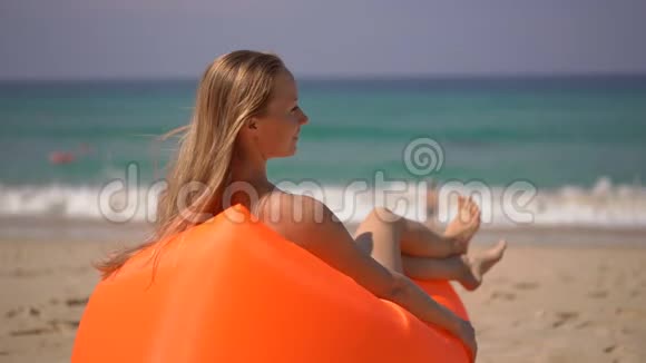 一位年轻女子在一张充气沙发上在热带海滩上放松的超慢镜头视频的预览图