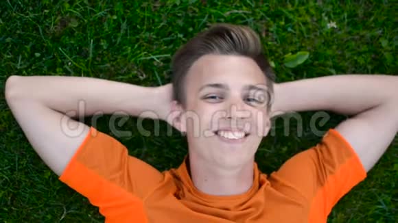 快乐的少年微笑着对着镜头在户外草地上休息视频的预览图