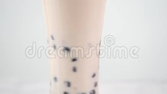在明亮的大理石桌面白色托盘上用玻璃杯搅拌美味的台湾大众饮料木薯珍珠泡奶茶视频的预览图