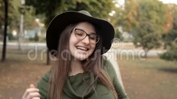 美丽的年轻女孩在外面的公园里跳舞快乐秋天一个戴着帽子戴着眼镜的女孩视频的预览图
