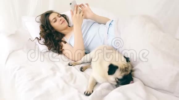 美孚电话用户女人在床上与她有趣的小巴格狗录像片段周末放松时刻视频的预览图