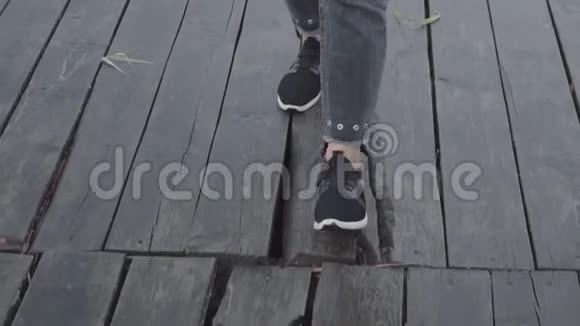 穿着运动鞋和黑裤子的女人走在潮湿的木板码头上视频的预览图