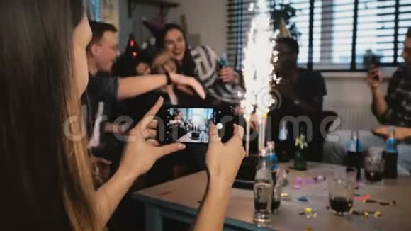 女性手拿智能手机拍照多民族生日派对配上烟火蜡烛朋友拥抱慢动作视频的预览图