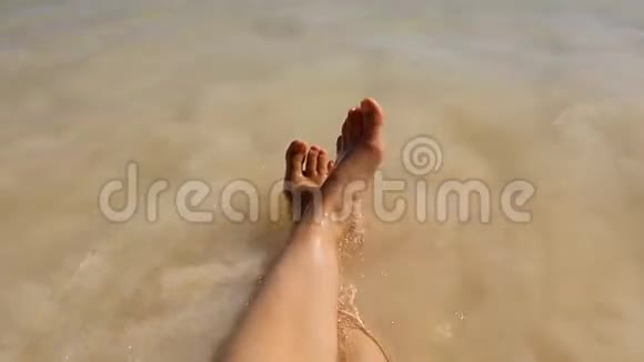 温暖平静的大海的海岸波浪洗了一个躺在海滩上的女人的两英尺视频的预览图