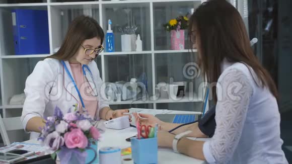 女医生测量病人在诊所办公室的压力并正在写她的任务视频的预览图