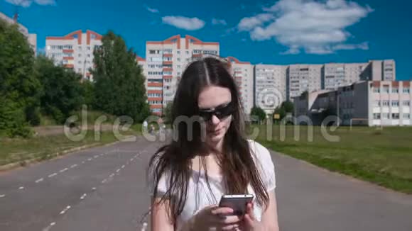 年轻的黑发女孩在住宅区的体育场里散步用手机说话视频的预览图