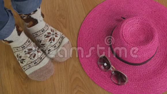 一个女人的腿坐在地板上穿着温暖的羊毛袜子附近有一顶宽边的粉红色帽子和太阳镜视频的预览图