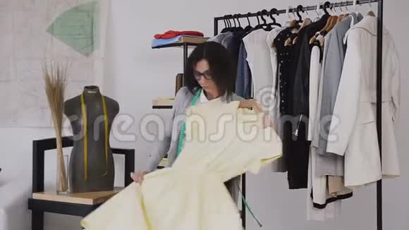 一个快乐的黑发女人正在做一件合适的黄色连衣裙这是在时装设计师工作室的衣架上服装视频的预览图