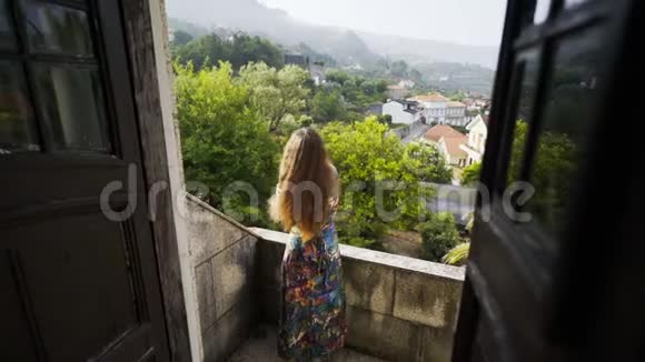 村中山丘之间别墅阳台上的年轻女士视频的预览图