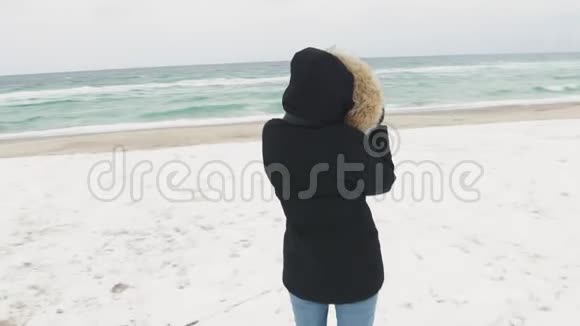 在寒冷的冬天年轻漂亮的女人在大海上拍照慢动作视频的预览图