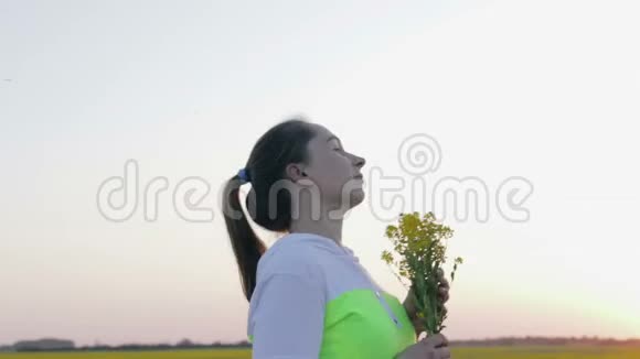 一个年轻的女人带着一束来自菜籽油的鲜花在夕阳下散步视频的预览图