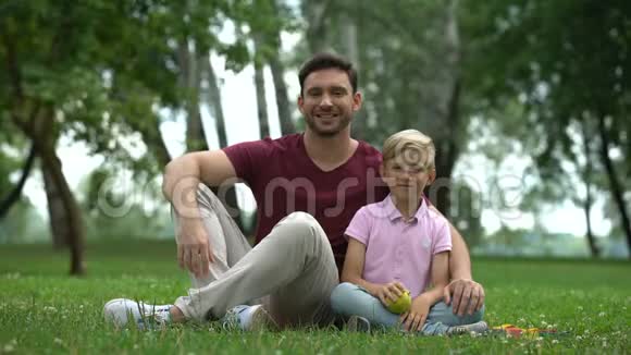 男孩和父亲坐在公园里把新鲜的苹果放进相机健康的食物视频的预览图