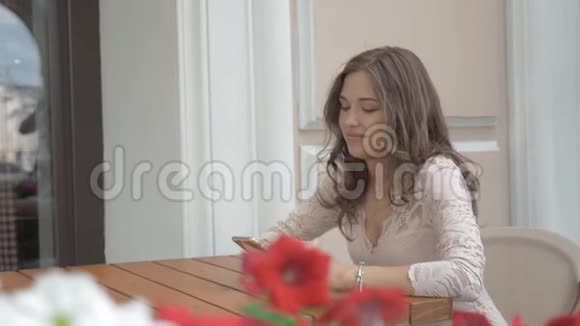 一个漂亮的女孩坐在街头咖啡馆里使用智能手机微笑好心情视频的预览图
