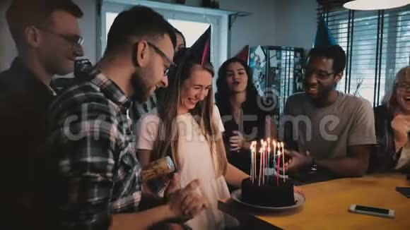 快乐的白人女孩在生日蛋糕上用蜡烛许愿多种族的朋友在惊喜派对慢动作视频的预览图