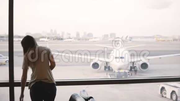美丽的女游客站在机场候机楼的窗口看飞机然后拿着包离开视频的预览图