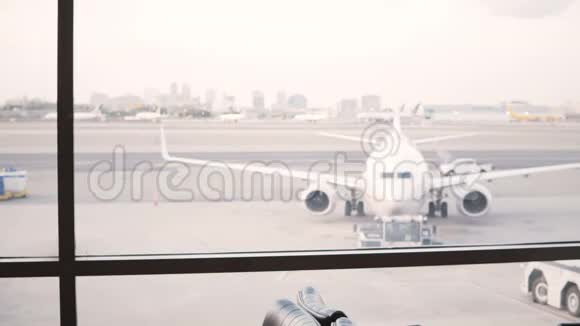 无法辨认的女旅行者带着袋子走到机场休息室候机室窗口欣赏飞机的景色视频的预览图