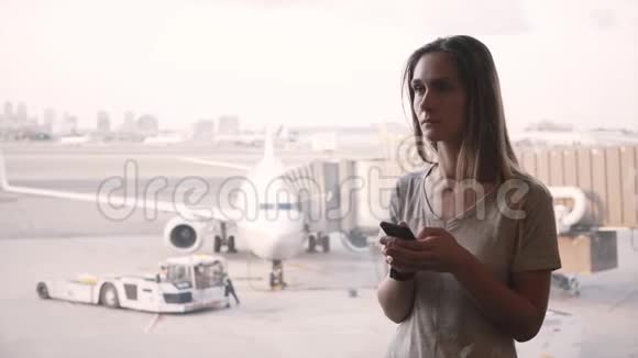 年轻的高加索女性旅行者使用智能手机听了机场窗口附近的公告后感到沮丧视频的预览图