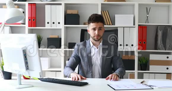 穿着灰色夹克的导演坐在白色办公室的桌子上消极地摇头视频的预览图