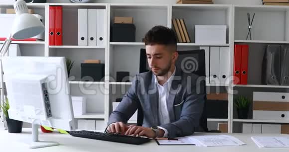 穿着灰色夹克的商人坐在白色办公室的桌子上在键盘上打印扔文件视频的预览图