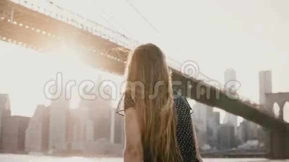 在布鲁克林大桥4K附近的河堤围栏旁风吹着头发的美丽女孩的后景视频的预览图