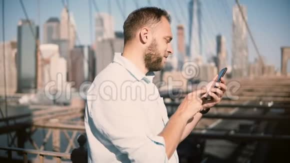 快乐的欧洲商人使用智能手机移动办公应用程序在布鲁克林大桥然后转向远离相机4K视频的预览图