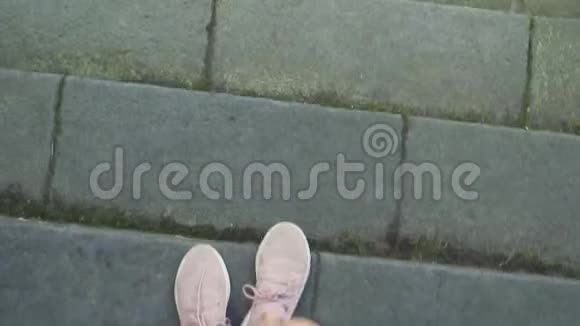 穿着粉色运动鞋的女性双腿走在铺有青草和落叶的鹅卵石路面上第一人称景观视频的预览图