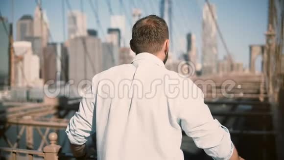 从后视图的成年白种人男子站在布鲁克林大桥栏杆享受惊人的城市景观和步行4K视频的预览图
