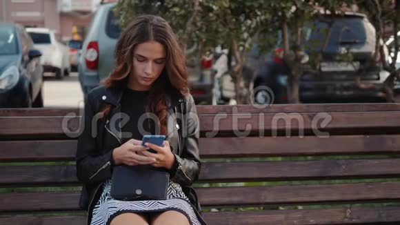 一个阳光明媚的少年坐在公园的长椅上一个漂亮开朗的女孩带着智能手机网上购物的概念视频的预览图