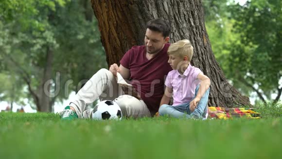 爸爸和儿子一起在公园看书一起准备作业做父母视频的预览图