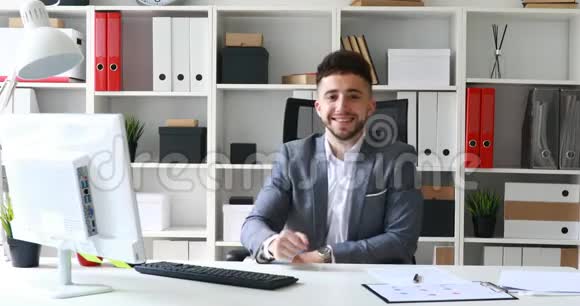 年轻的商人坐在白色的办公室里微笑着摆出赞许的手势视频的预览图