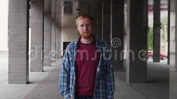 一个年轻人在柱子背景上的肖像一个年轻人站在大楼旁边的街道上严肃的表情视频的预览图