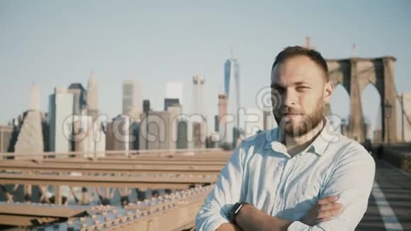 成功快乐的欧洲商人的肖像双臂交叉微笑回首纽约布鲁克林大桥视频的预览图