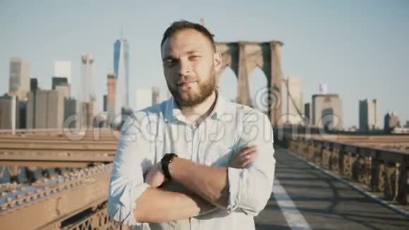 年轻的积极的男性白种人商人双臂交叉看着相机微笑着在布鲁克林大桥纽约4K视频的预览图