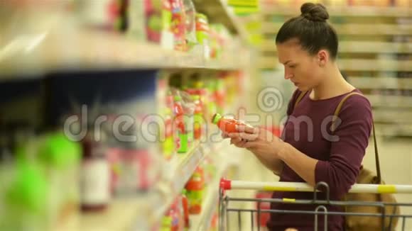 年轻女子从超市货架上挑选果汁她的超市里有很多东西视频的预览图