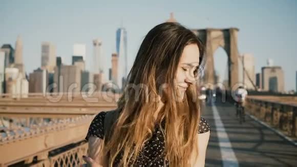 美丽的白种人女孩享受温暖的阳光天气转过头看着镜头微笑布鲁克林大桥4K视频的预览图