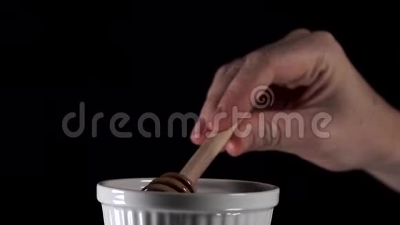 女性用蜂蜜勺从黑色背景的白色盘子中捞出蜂蜜视频的预览图