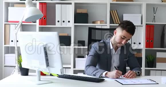 穿着灰色夹克的商人坐在白色办公室的桌子上签署文件制作纸飞机视频的预览图