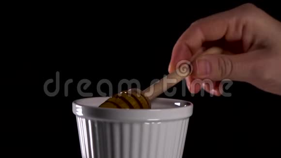 女性用蜂蜜勺从黑色背景的白色盘子中捞出蜂蜜视频的预览图