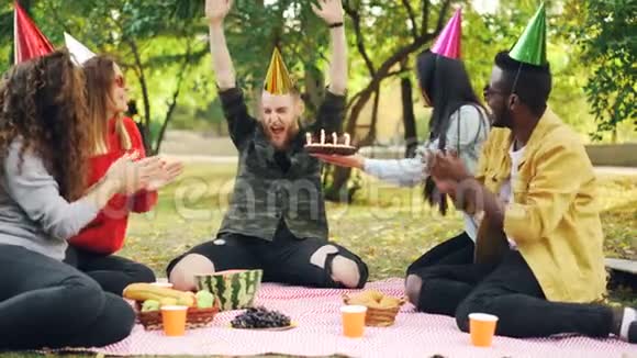 大胡子男和公园里的朋友一起庆祝生日在蛋糕上吹蜡烛大声喊叫表达积极的态度视频的预览图