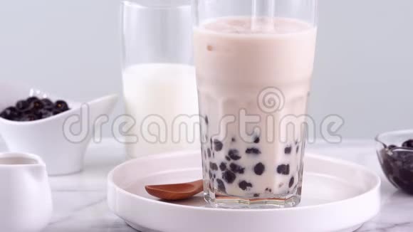 在明亮的大理石桌上的白色托盘上用玻璃杯搅拌美味的台湾大众饮料木薯珍珠泡奶茶视频的预览图