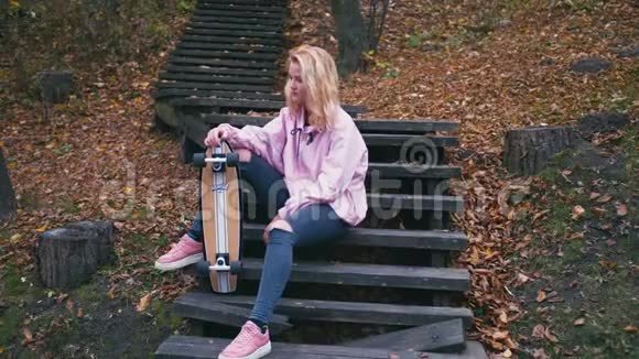 漂亮的金发女郎和滑板长板在森林里摆姿势视频的预览图