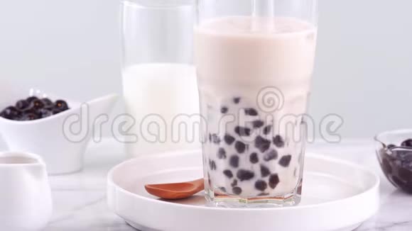 在明亮的大理石桌上的白色托盘上用玻璃杯搅拌美味的台湾大众饮料木薯珍珠泡奶茶视频的预览图