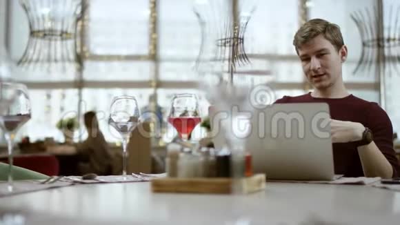 一个年轻的商人坐在一家咖啡馆的桌子旁用iphone一边笑一边看着过路人视频的预览图
